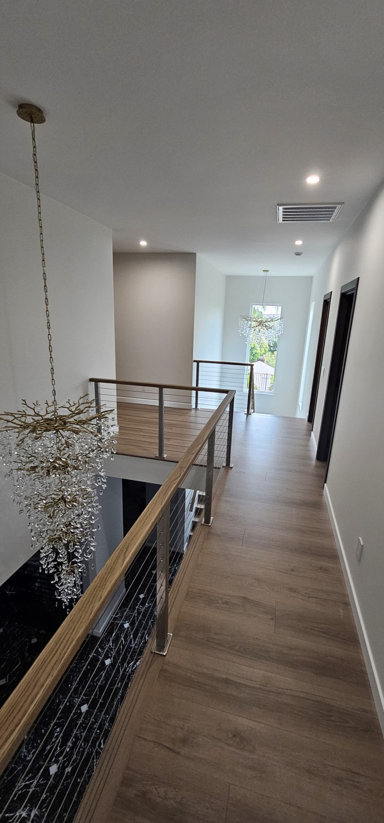 Second-floor hallway with cable railing and chandelier in a home addition by Idea Fix Construction