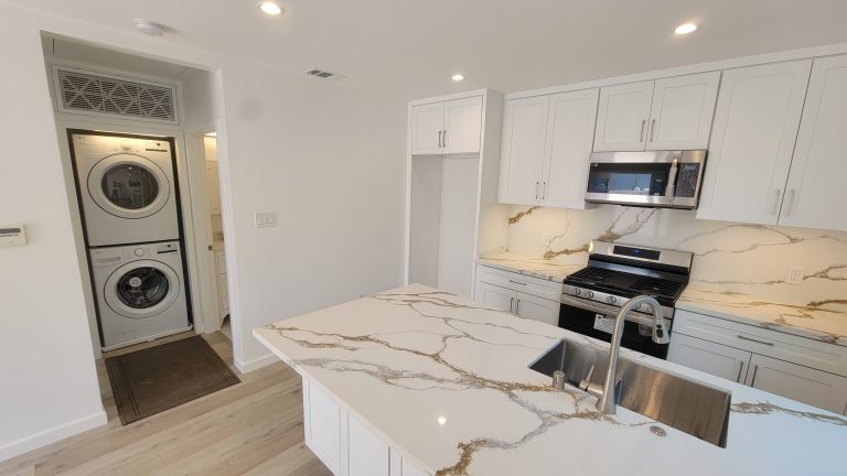 Remodeled kitchen with quartz island, stainless appliances and stacked laundry by Idea Fix Construction